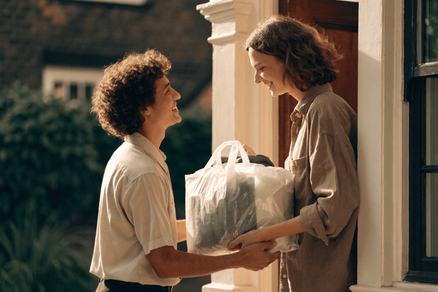 Delivery person handing clean laundry to a customer at their door
